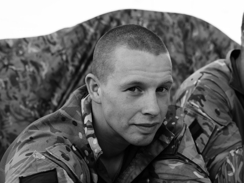Jack Charman, founder and chief investigator at National Private Investigators. Dressed in his military camouflage uniform sitting with arms resting on knees.