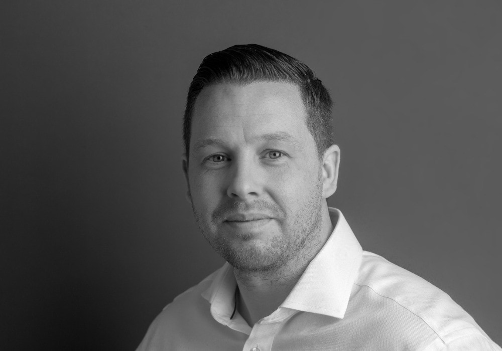 Black and white portrait of a man in a white collared shirt, looking at the camera with a neutral expression against a plain background