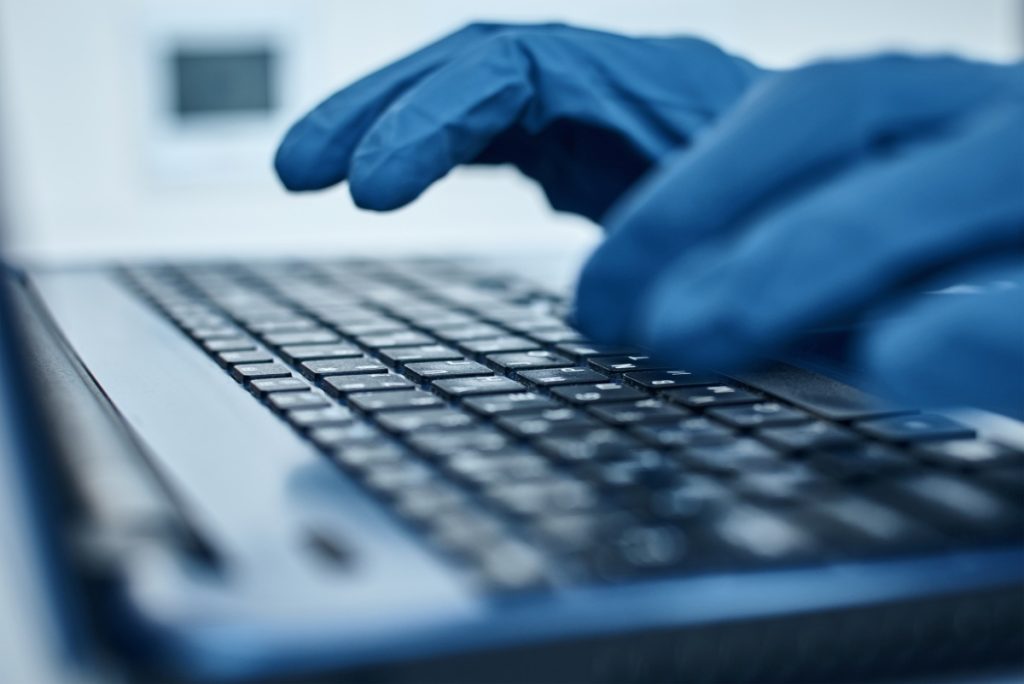 Hand in protective gloves typing on the laptop keyboard